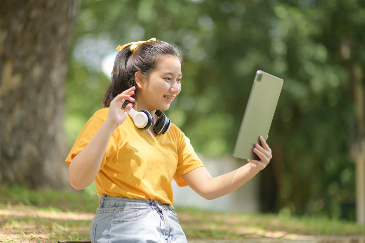 Asian Teen Girl Greets Her Friends with a Tablet.